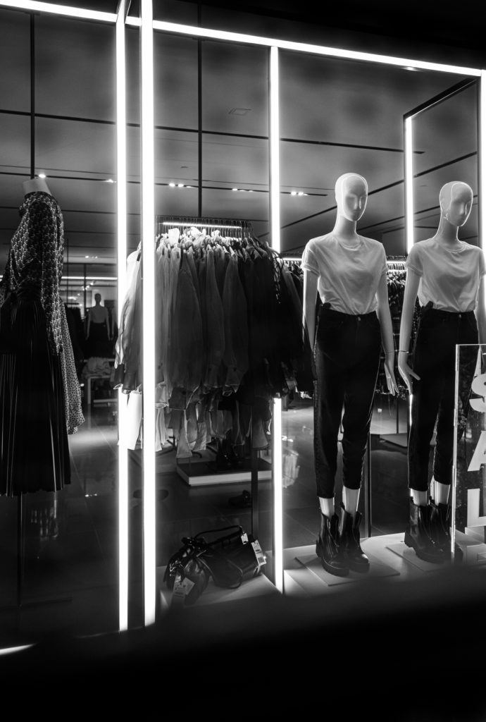 Dark black and white image of a woman's store, with floor lighting. around the bottom of a display with two models dressed in combat boots with white t-shirts.